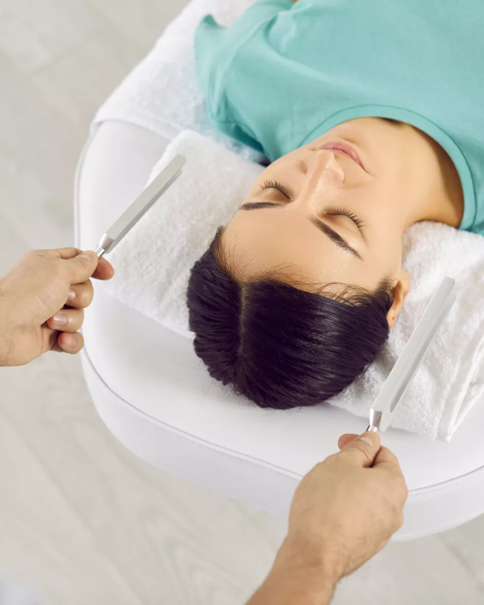 Does Biofield Tuning work? A client lying down with her eyes closed while tuning forks are held near her head
